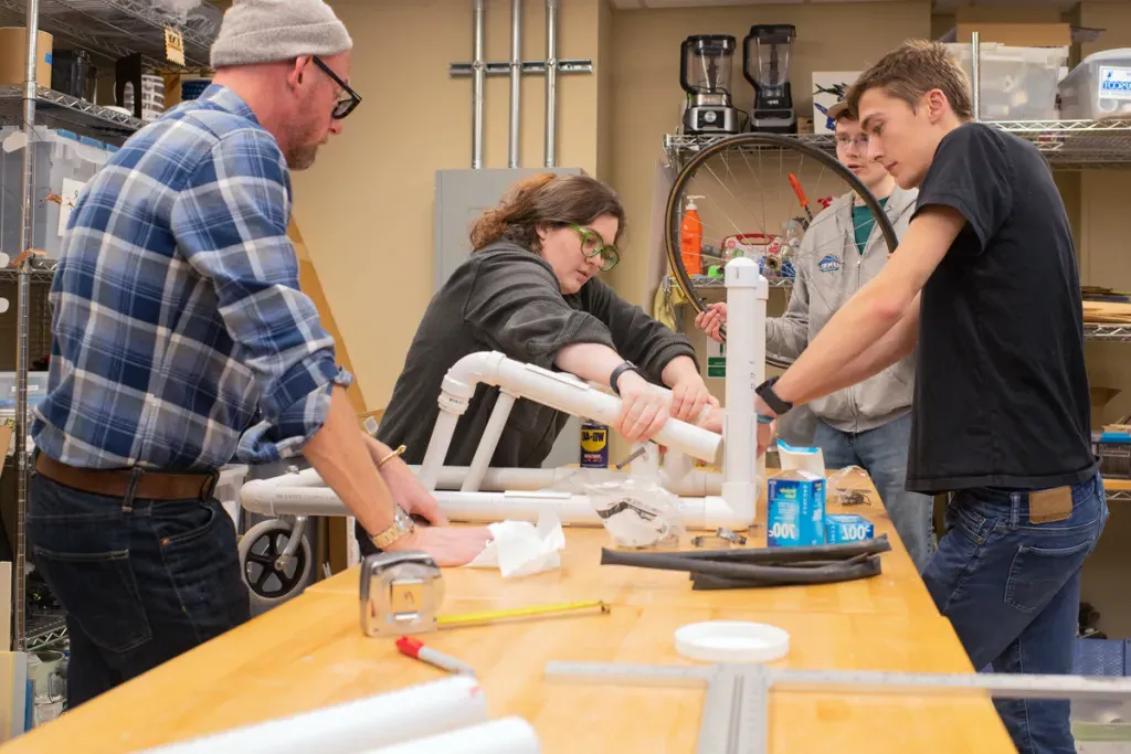 Three students and a professor assemble part of a wheelchair together